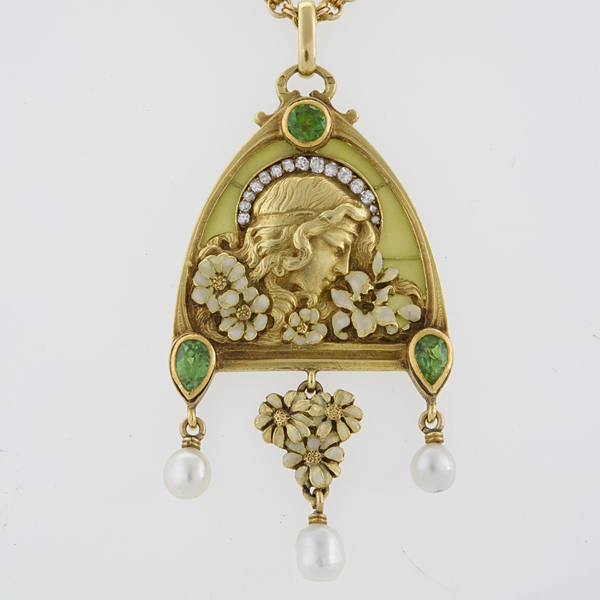 A gold piece of jewelry with decorative flowers, a face in profile, and pearls dangling from emeralds.