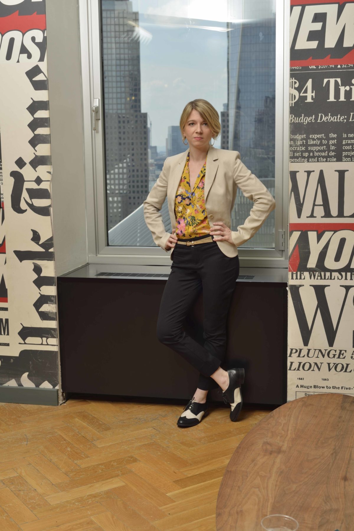 The president of Poster House posing in front of a window that is in between newspaper posters.