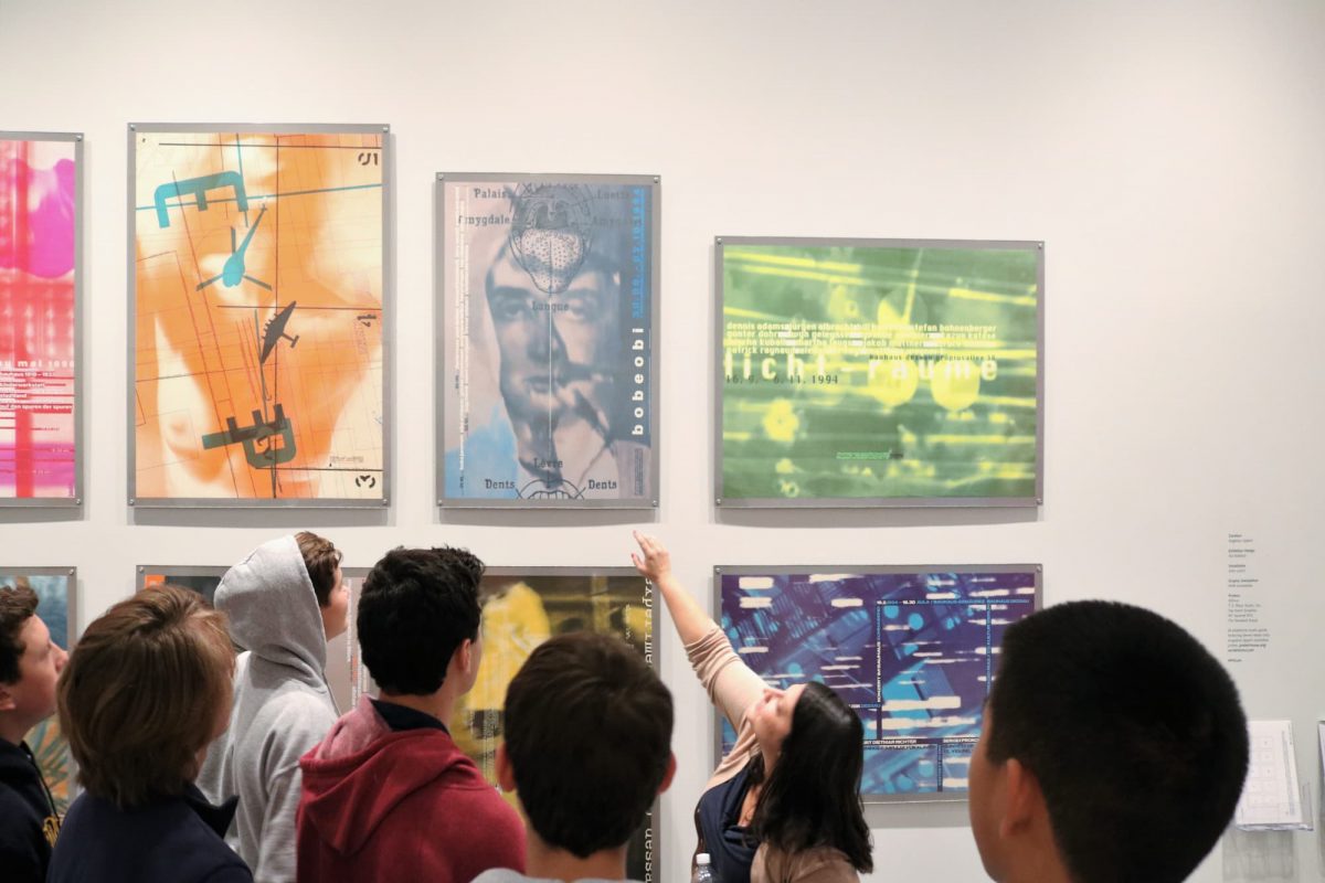 photograph of students standing around while an educator points at posters