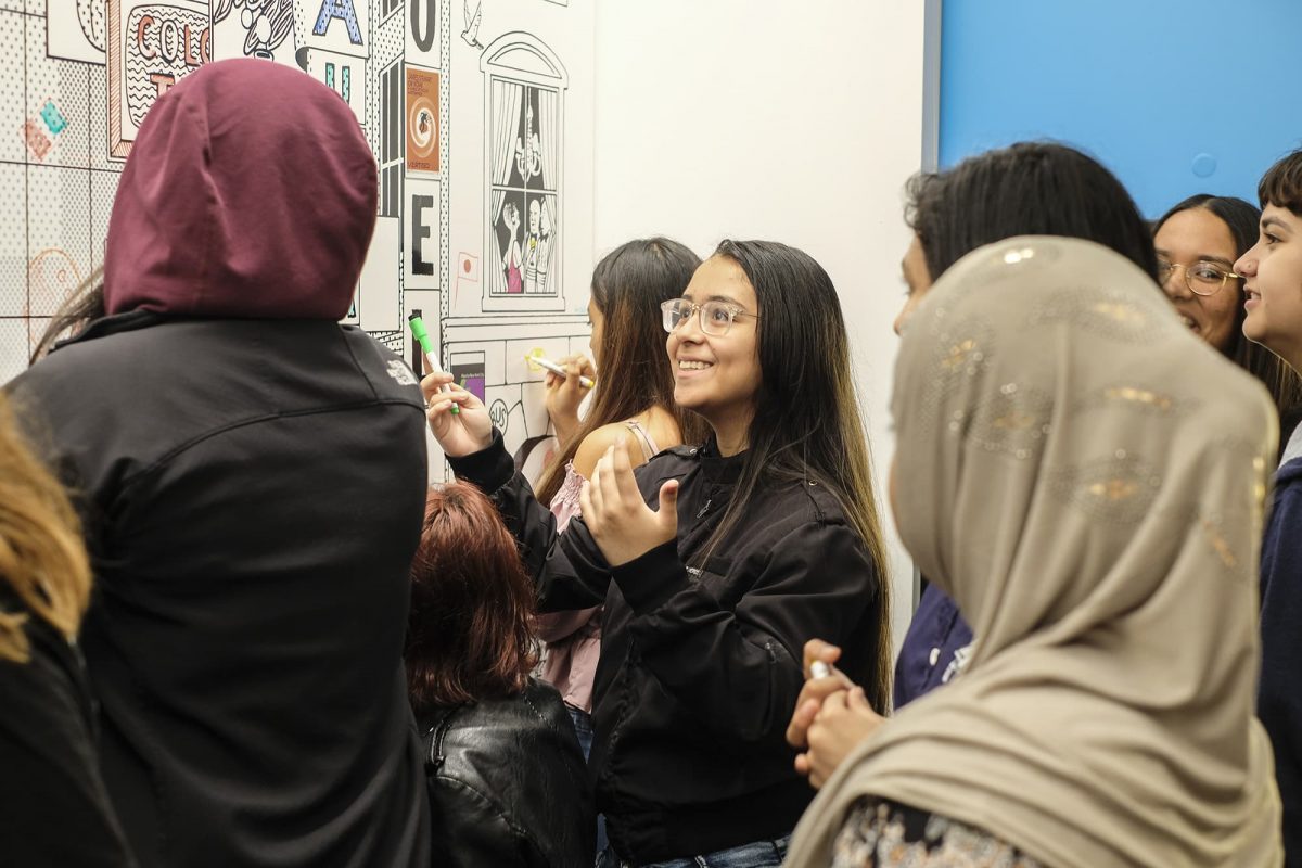 photograph of a group of students gathered around and drawing on a dry erase board