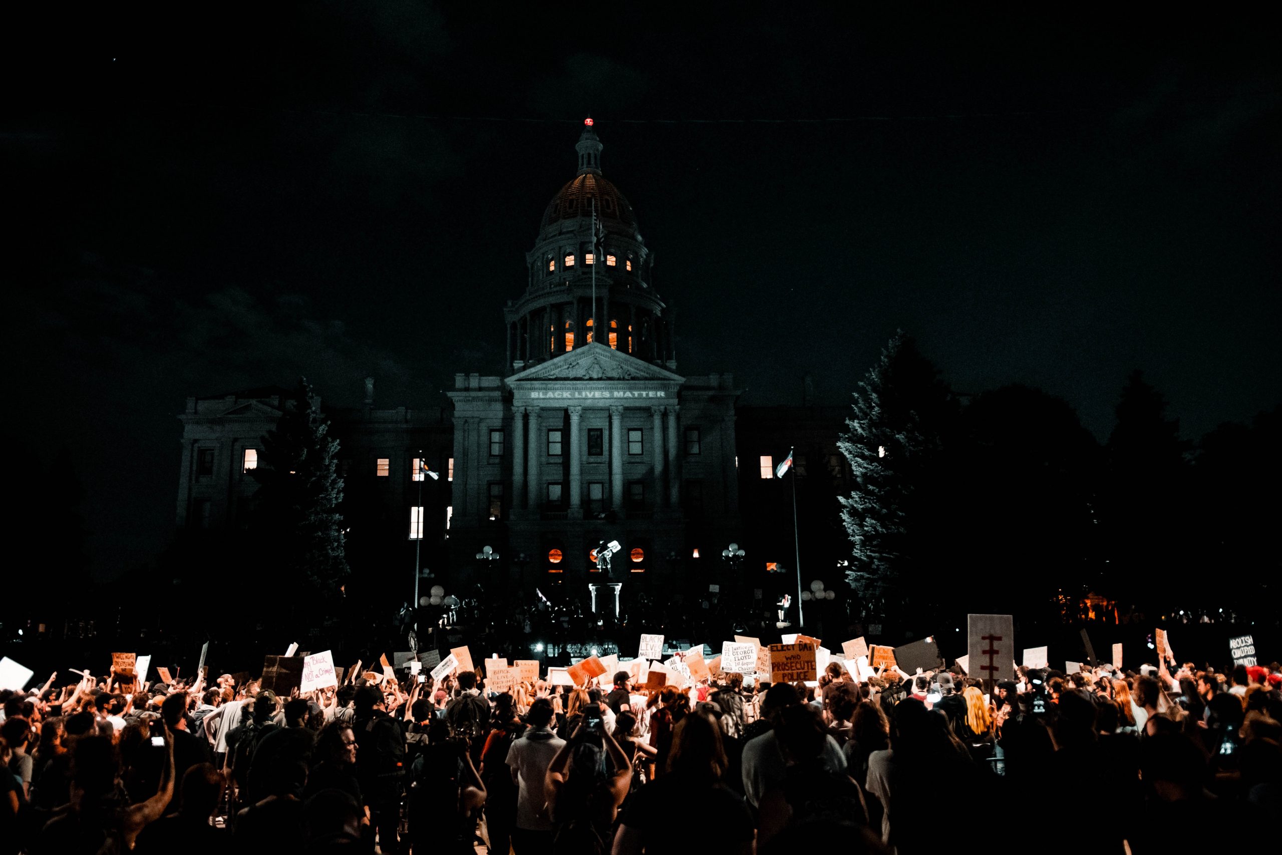 Black Lives Matter protesters rally in front of a building with the words 