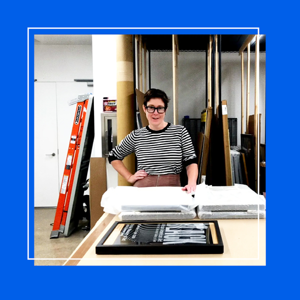 The archives room featuring the Collections Manager with covered art pieces in the center looking at the camera within a blue frame.