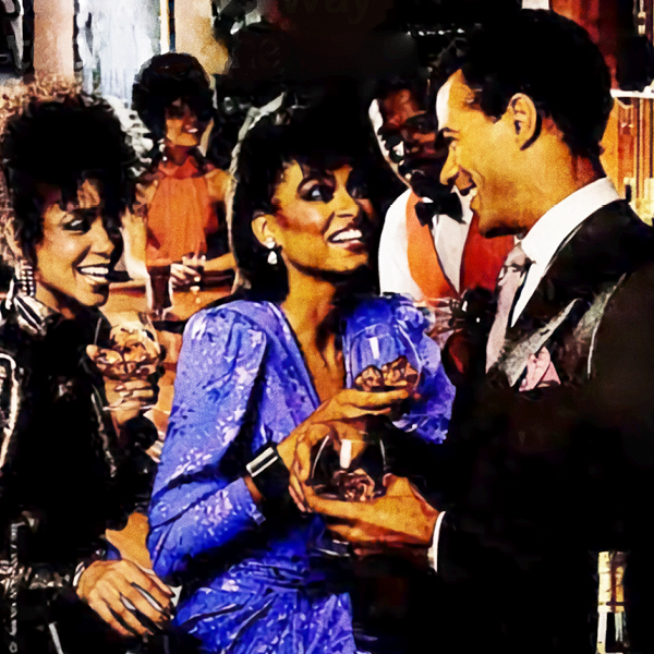 A cropped image featuring two black women and a black man laughing and drinking in a bar.