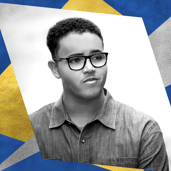 A black and white headshot of a person with glasses and a denim shirt on a trapezoid shaped background.