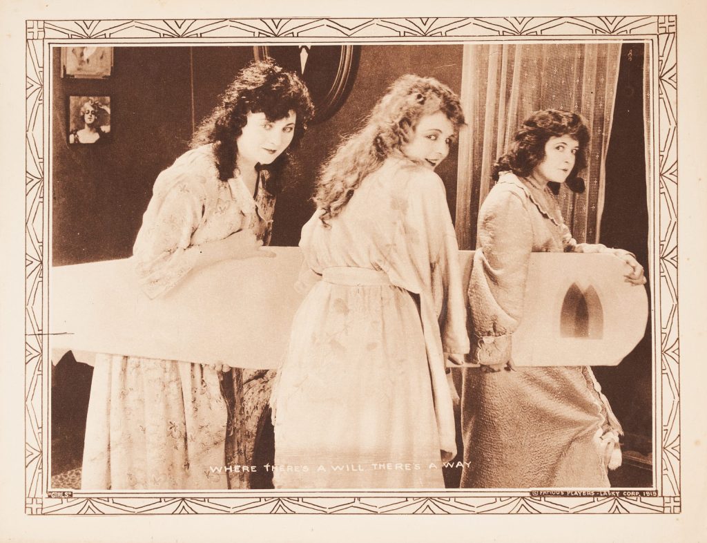 A lobby card featuring three women carrying a large object.