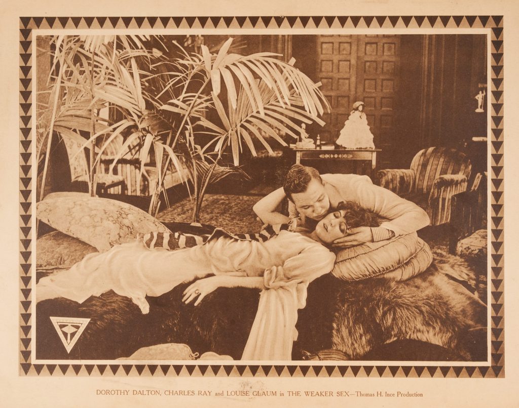 photographic image of a woman in a dress laying down on pelts while a man tries to revive her