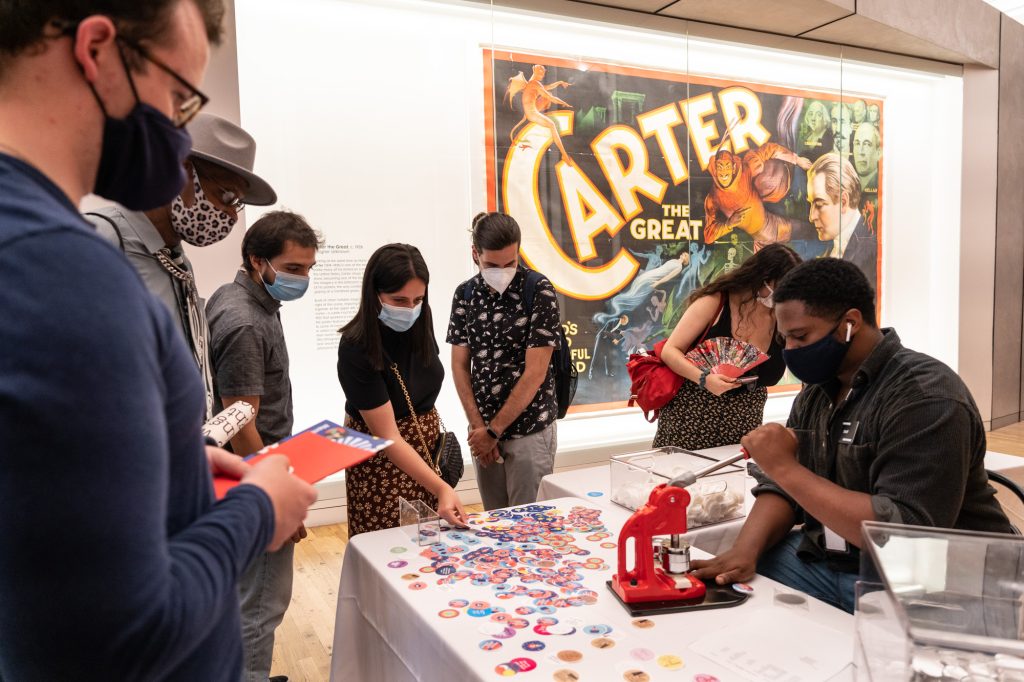 A group of people watching a person make buttons with a button maker.