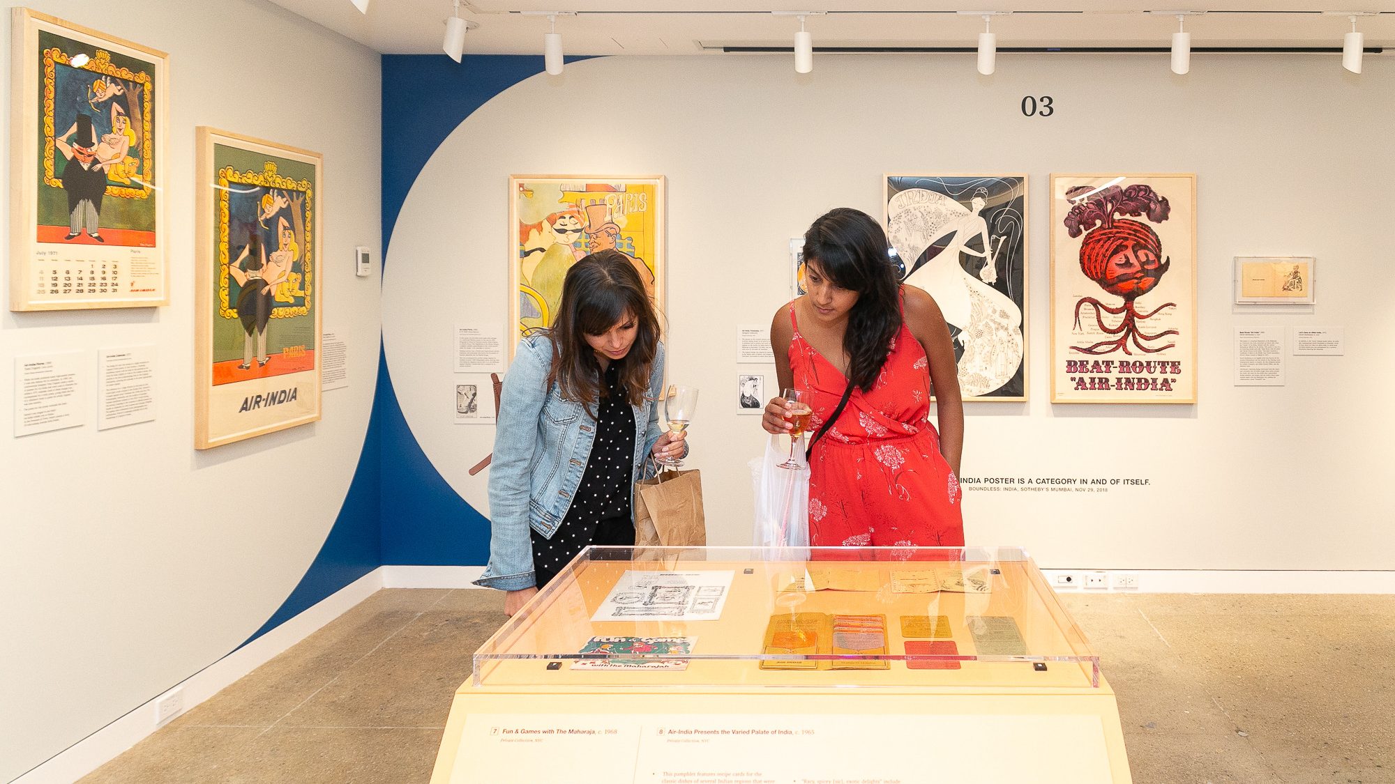 Two visitors standing in a gallery, looking down at a case containing works on paper.