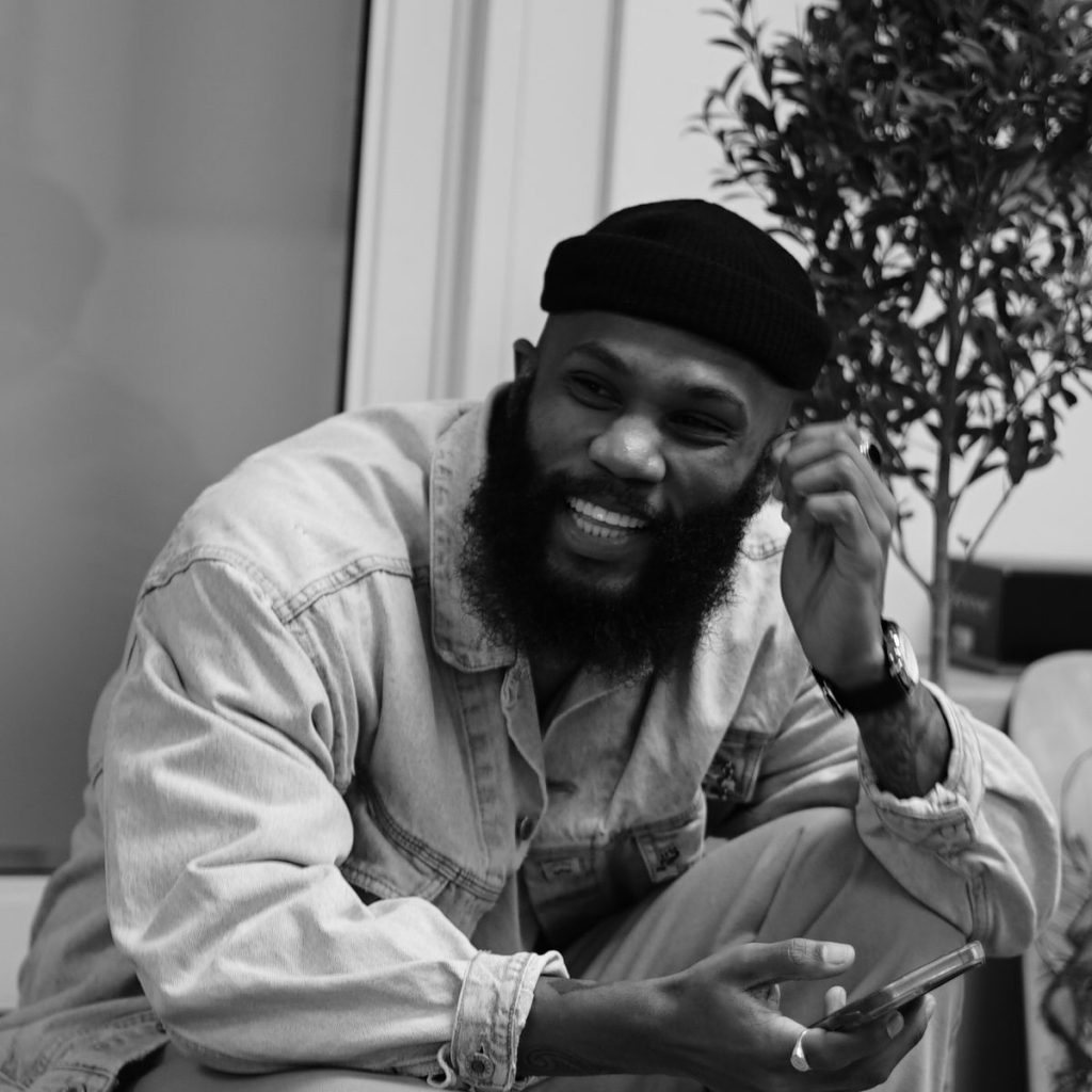 A black and white photo of a Black man with a full beard wearing a black beanie.