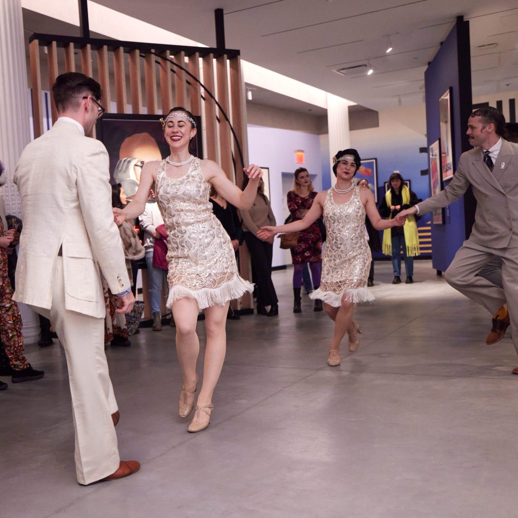a photograph of people dancing in 1920s flapper costumes in Poster House's main gallery.