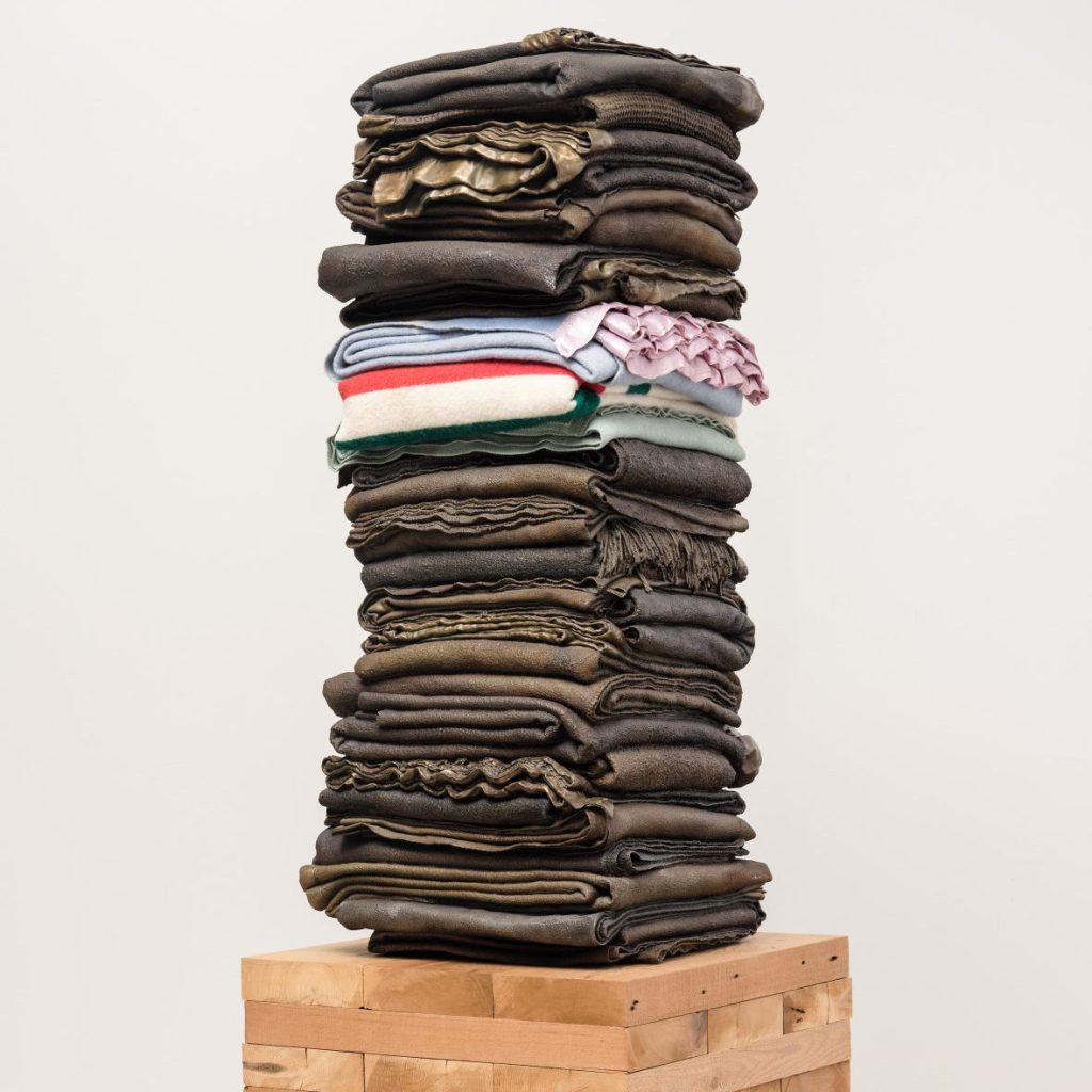 A stack of faded jeans stand on a box in an art gallery.