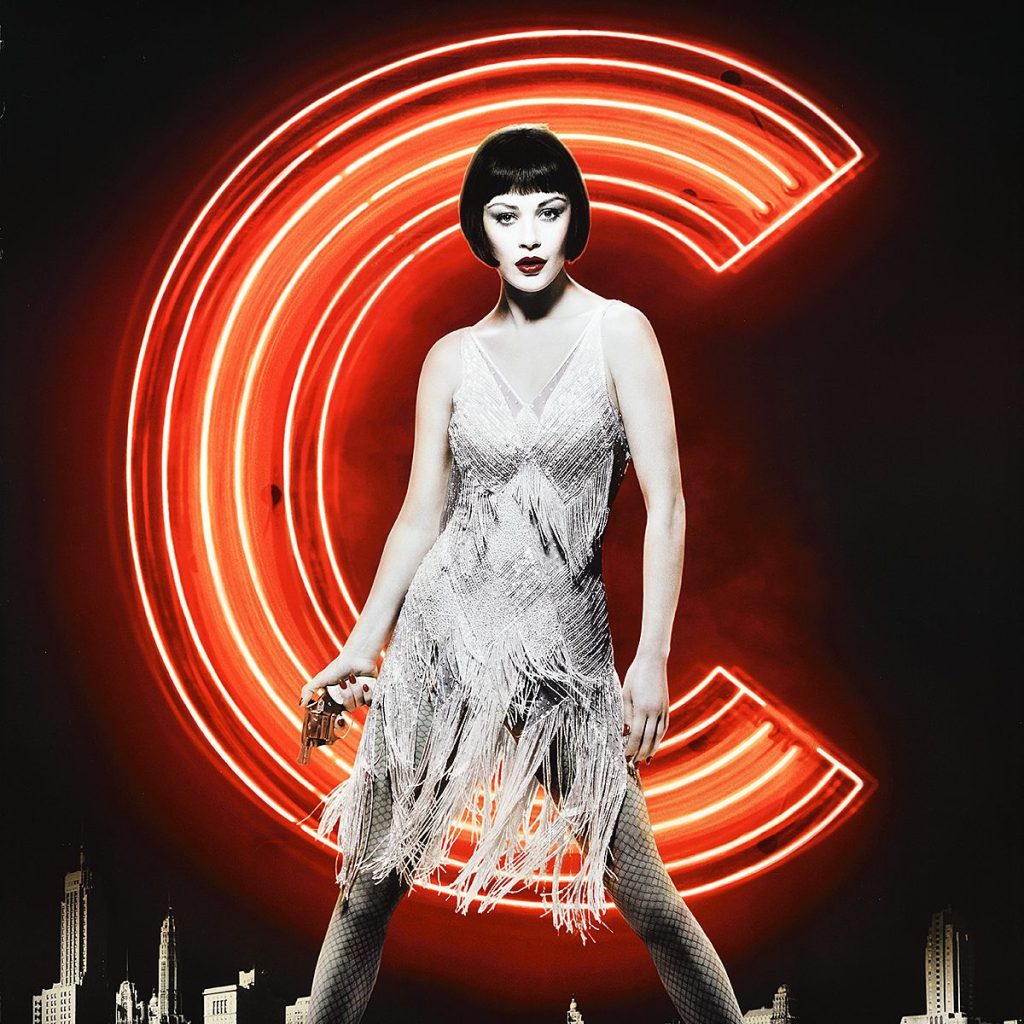 A woman in a flapper costume stands in front of a neon letter C