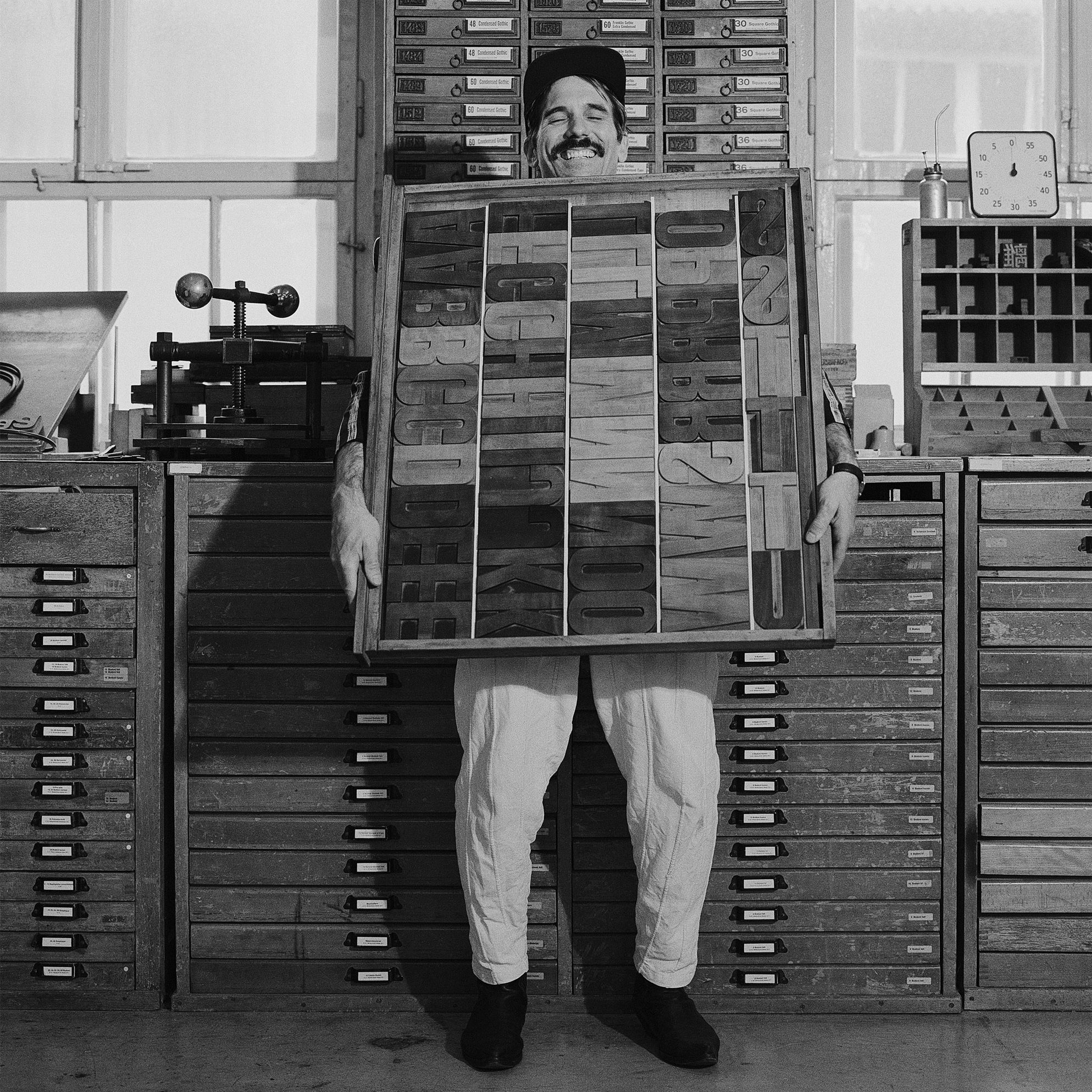 A photo of man in a foundry holding examples of several letterpresses