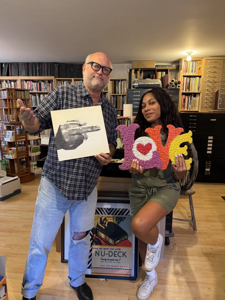 Photograph of a young woman and an older man holding up prints.