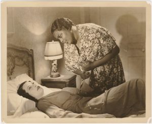 Vintage image of a woman looking down at a woman lying down on a bed.