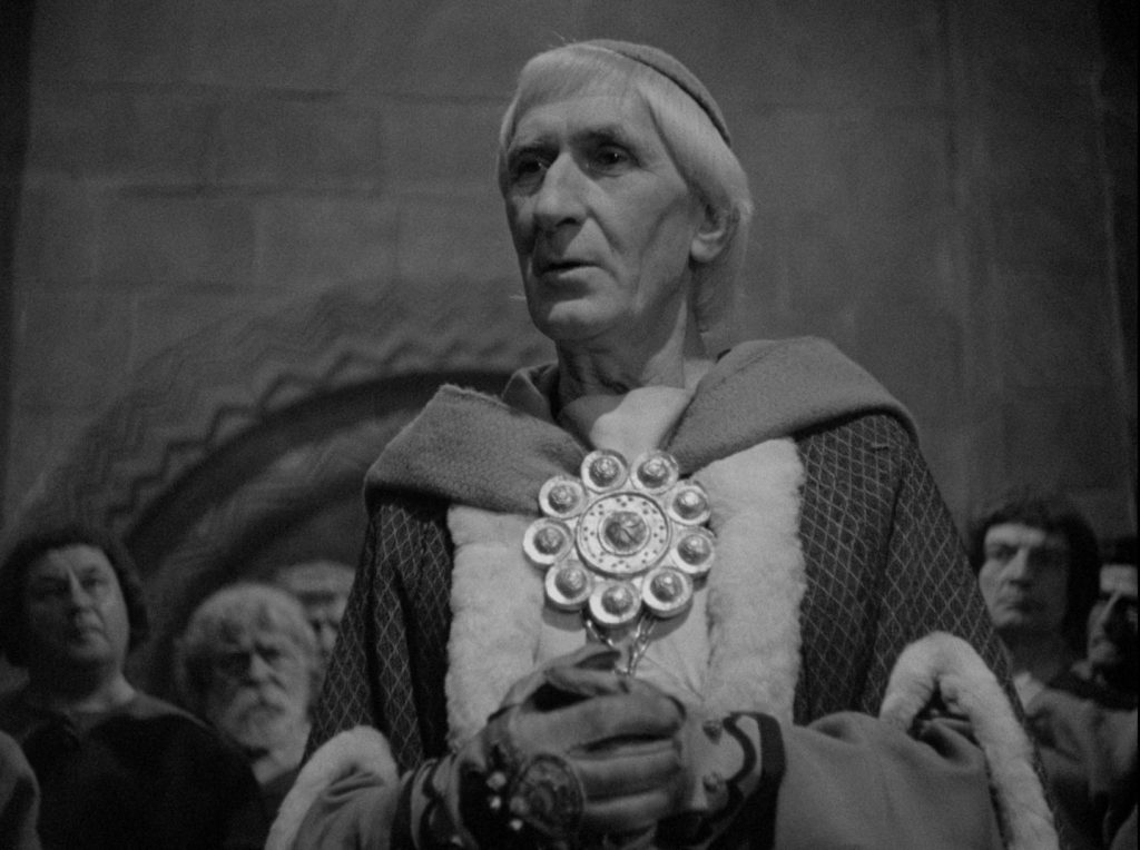 Black and white image of an elderly man in medieval attire holding a large, ornate medallion.
