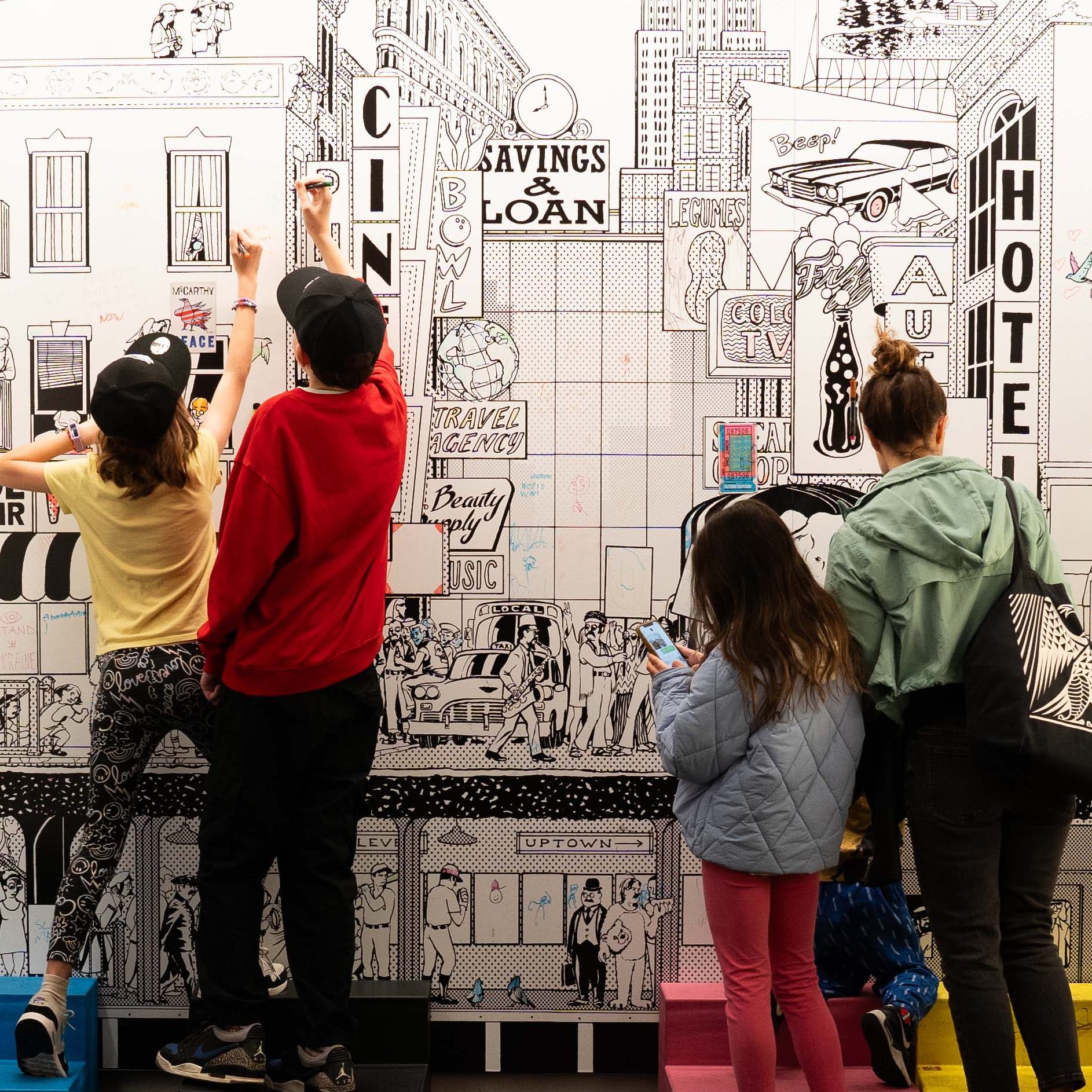 four people standing coloring on a wall that has a cityscape mural on it